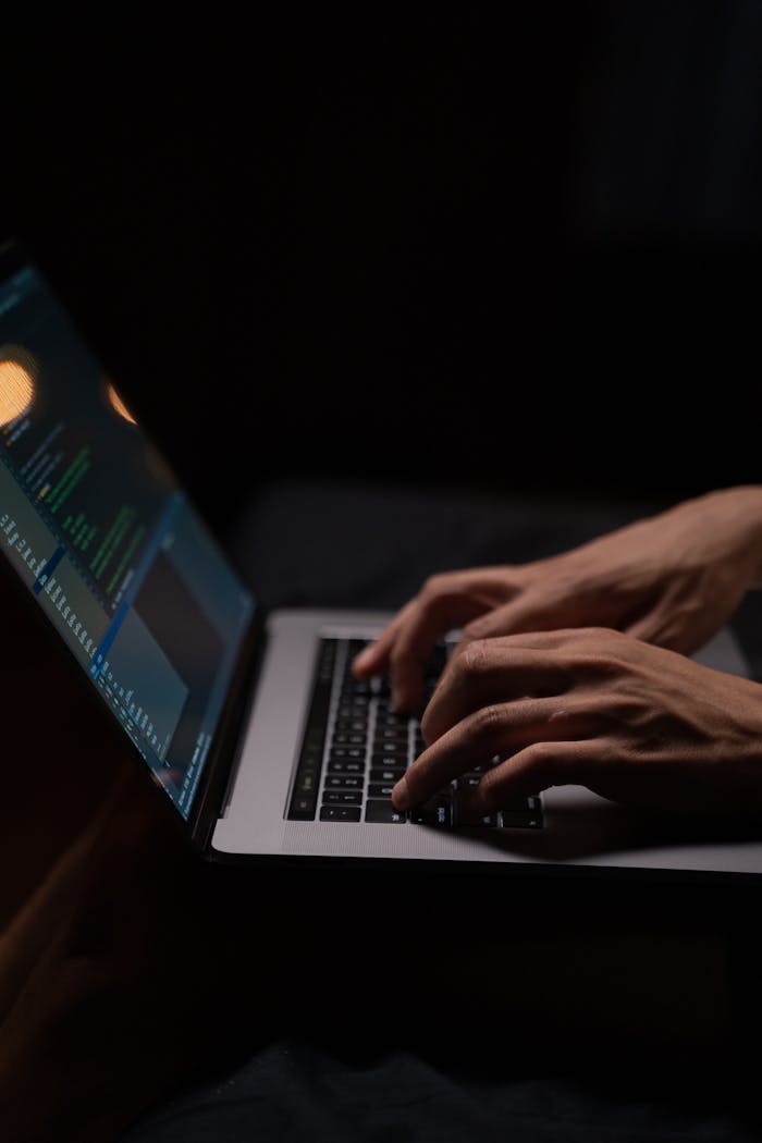 service-05 Hands typing code on a laptop keyboard in a dark room, capturing the essence of late-night programming.